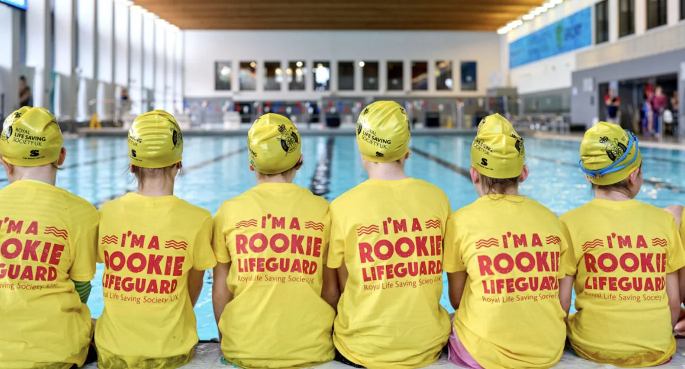 Rookie Lifeguard participants in yellow shirts sitting beside the pool